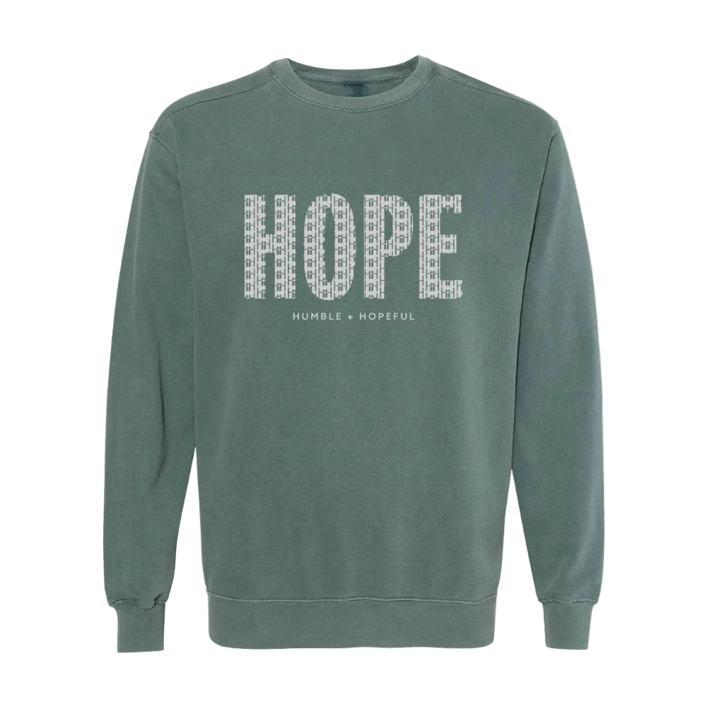 A muted blue spruce crewneck sweatshirt featuring the word 'HOPE' printed across the chest in a white patterned font, with 'HUMBLE + HOPEFUL' written underneath.