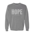 A gray crewneck sweatshirt featuring the word 'HOPE' printed across the chest in a white patterned font, with 'HUMBLE + HOPEFUL' written underneath in smaller text.