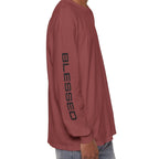 A man shown from the side wearing a brick long-sleeve t-shirt with 'BLESSED' printed vertically in black on the sleeve, paired with light blue jeans against a plain white background.