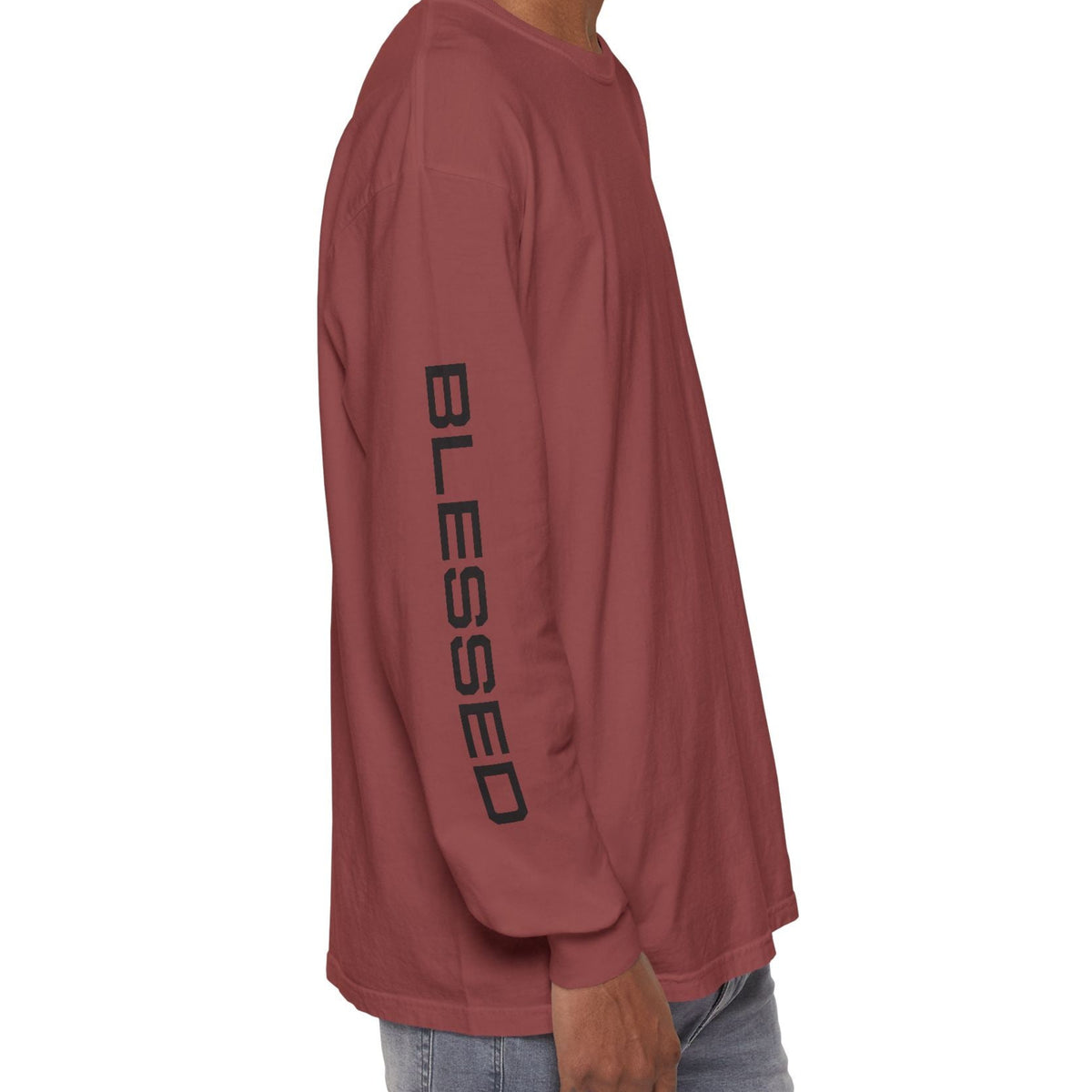 A man shown from the side wearing a brick long-sleeve t-shirt with 'BLESSED' printed vertically in black on the sleeve, paired with light blue jeans against a plain white background.