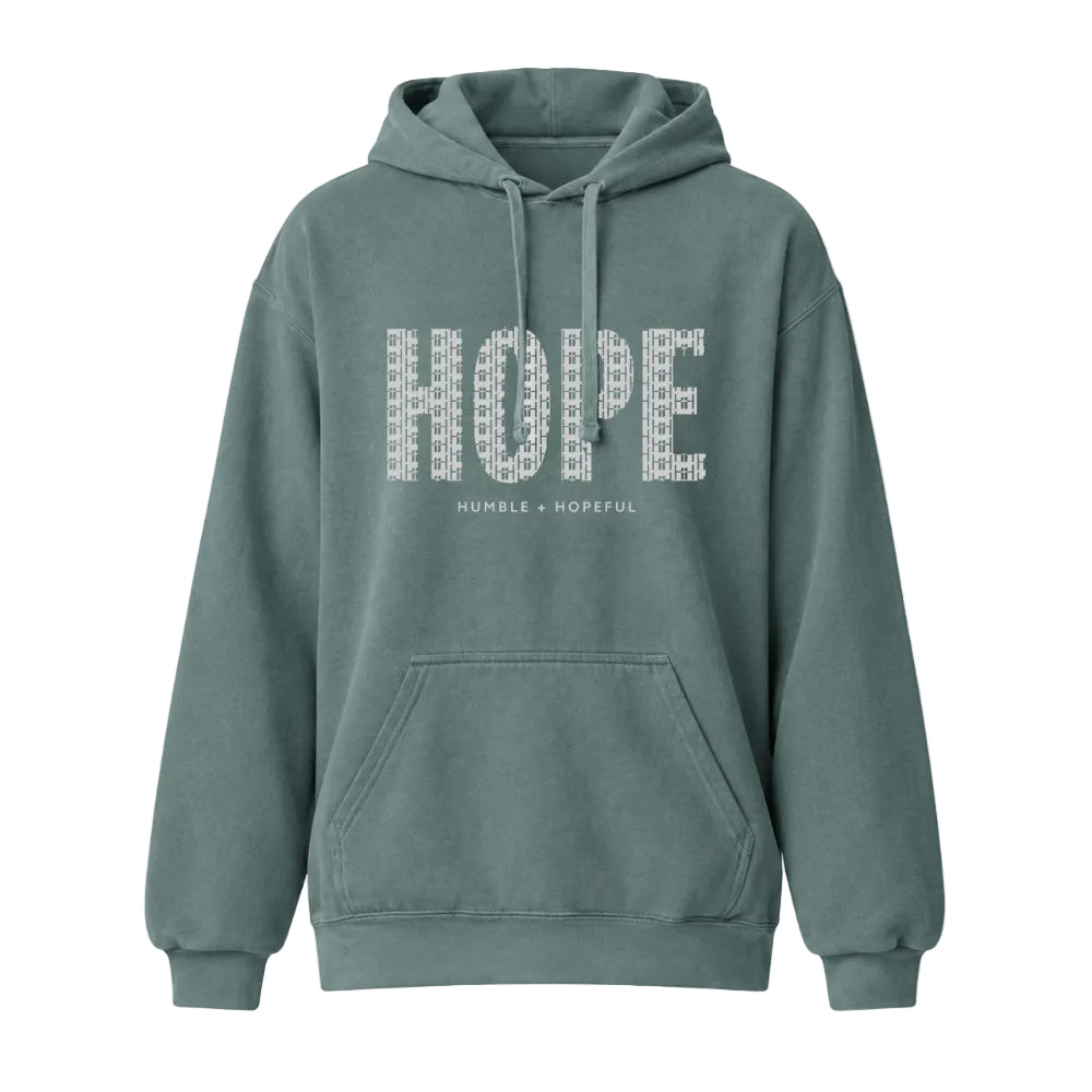 A blue spruce pullover hoodie with a front kangaroo pocket and drawstrings, featuring the word 'HOPE' printed in a white geometric pattern across the chest, with 'HUMBLE + HOPEFUL' underneath.