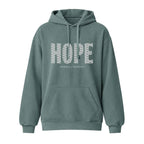 A blue spruce pullover hoodie with a front kangaroo pocket and drawstrings, featuring the word 'HOPE' printed in a white geometric pattern across the chest, with 'HUMBLE + HOPEFUL' underneath.