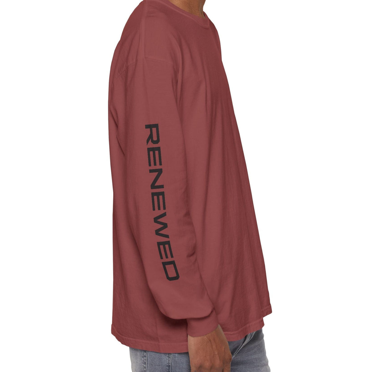 A man shown from the side wearing a brick long-sleeve t-shirt with 'RENEWED' printed vertically in black on the sleeve, paired with light blue jeans against a plain white background.