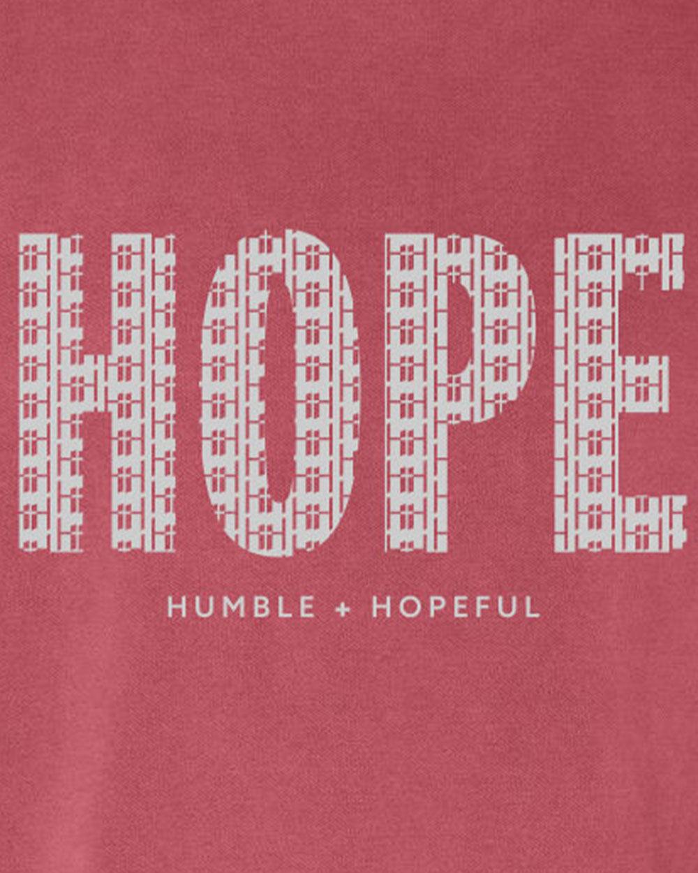 A close-up of a crimson fabric surface with large white block letters spelling 'HOPE' and smaller text below reading 'HUMBLE + HOPEFUL'.