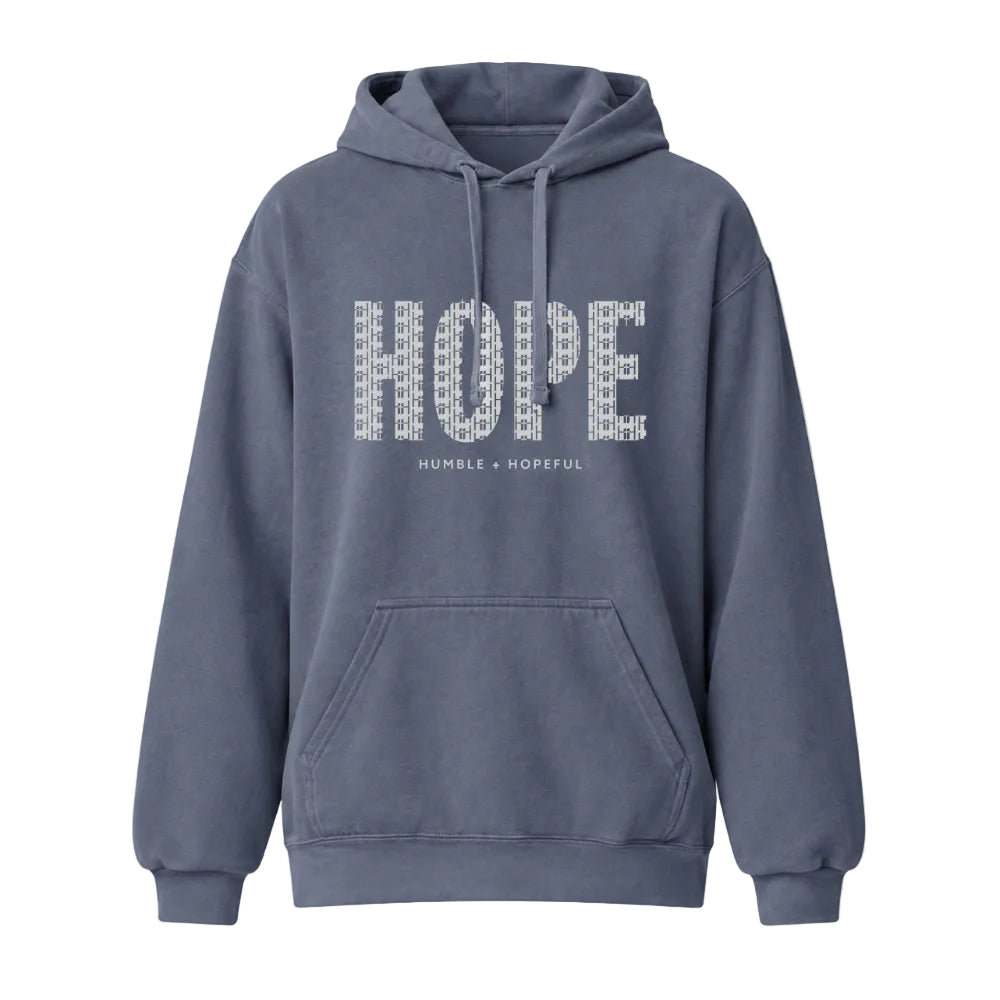 A denim color pullover hoodie with a front kangaroo pocket and drawstrings, featuring the word 'HOPE' in a textured white pattern across the chest, with the smaller text 'HUMBLE + HOPEFUL' underneath.