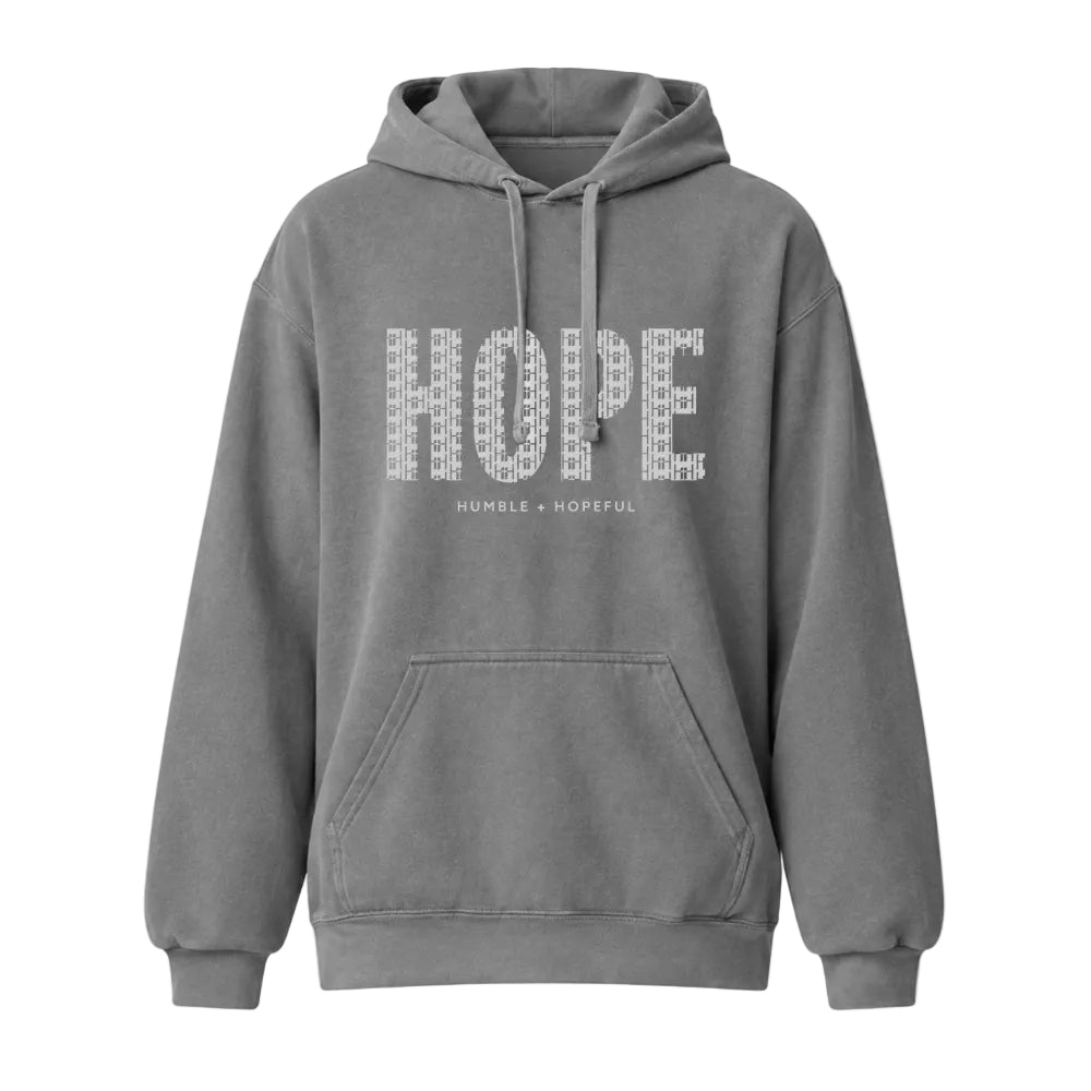 A gray pullover hoodie with a front kangaroo pocket and drawstrings, featuring the word 'HOPE' in a textured white pattern across the chest, with the smaller text 'HUMBLE + HOPEFUL' underneath.