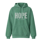 A green pullover hoodie with a front kangaroo pocket and drawstrings, featuring the word 'HOPE' printed across the chest in a white geometric pattern, with the text 'HUMBLE + HOPEFUL' underneath.