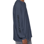 A man shown from the side wearing a slate blue long-sleeve performance shirt with 'BLESSED' printed vertically in black on the left sleeve, paired with light-wash jeans against a plain white background.