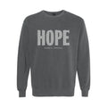 A dark gray crewneck sweatshirt featuring the word 'HOPE' printed across the chest in a white patterned font, with 'HUMBLE + HOPEFUL' written underneath in smaller text.
