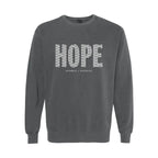A dark gray crewneck sweatshirt featuring the word 'HOPE' printed across the chest in a white patterned font, with 'HUMBLE + HOPEFUL' written underneath in smaller text.