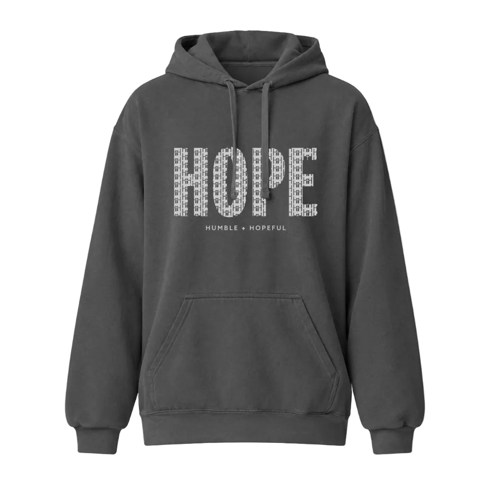 A dark gray pullover hoodie with a front kangaroo pocket and drawstrings, featuring a graphic on the chest that spells 'HOPE' in a patterned white font, with 'HUMBLE = HOPEFUL' printed underneath.