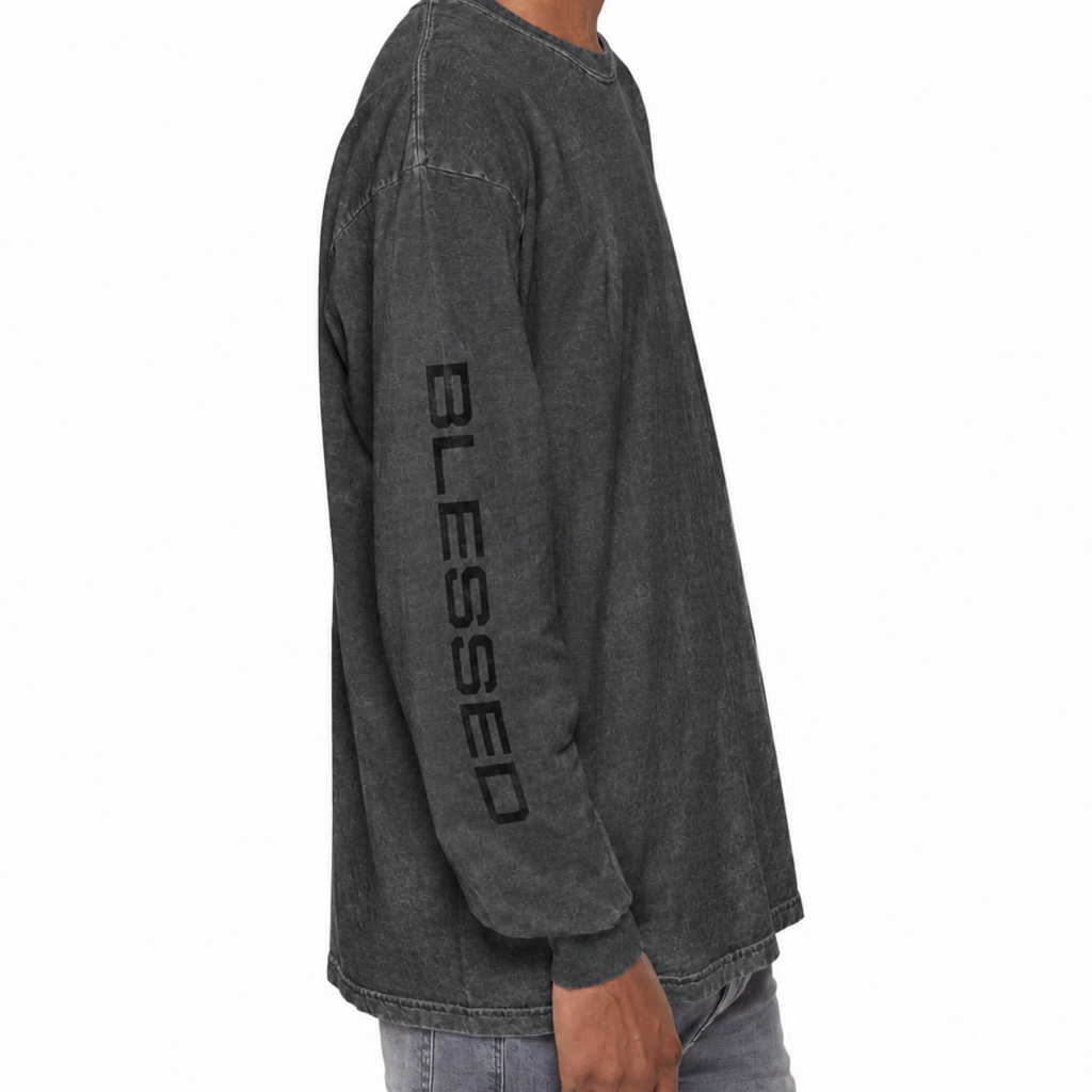 A man wearing a pepper gray washed long-sleeve t-shirt with 'BLESSED' printed vertically in black on the left sleeve, paired with light blue jeans, shown from a side profile against a white background.