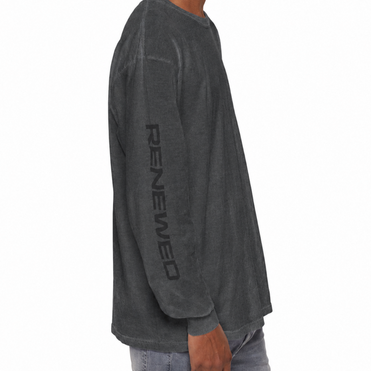 A man shown from the side wearing a dark charcoal gray long-sleeve t-shirt with 'RENEWED' printed vertically in black on the left sleeve, paired with light blue jeans against a plain white background.
