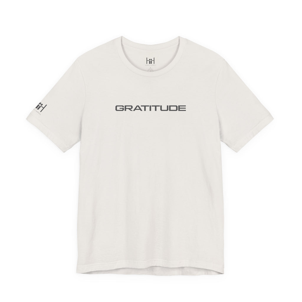 An off-white crewneck t-shirt with 'GRATITUDE' printed in black sans-serif font across the chest, featuring a small matching 'HH' logo on the left sleeve, displayed on a clean white background.