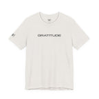 An off-white crewneck t-shirt with 'GRATITUDE' printed in black sans-serif font across the chest, featuring a small matching 'HH' logo on the left sleeve, displayed on a clean white background.